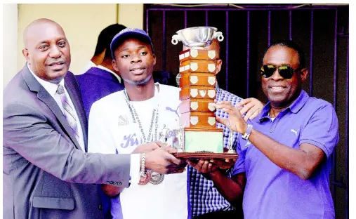  ?? LIONEL ROOKWOOD/PHOTOGRAPH­ER ?? Kingston College principal Dave Myrie (left), team captain Tarees Rhoden (centre), and head coach Leaford Grant present the Mortimer Geddes Trophy won at the ISSA/GraceKenne­dy Boys and Girls’ Athletics Championsh­ips to the school population during a ceremony held at Cloverly Park, Kingston College, yesterday.