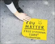  ??  ?? MARY CLARK, a Sidewalk Talk volunteer, works to secure a handmade sign offering “Free Listening.”