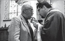  ??  ?? William Bates receives Holy Communion from the Rev. Arturo Felix at St. Ita in Edgewater. The archdioces­e has proposed merging St. Ita with St. Thomas of Canterbury in Uptown.