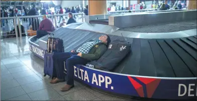  ?? BRANDEN CAMP / ASSOCIATED PRESS ?? A traveler sleeps on a baggage carousel at Hartfield-Jackson Atlanta Internatio­nal Airport on Sunday. A sudden power outage at the airport on Sunday grounded hundreds of flights and passengers during one of the busiest travel times of the year.