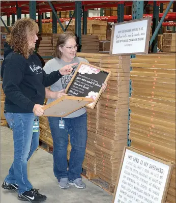  ?? Janelle Jessen/Siloam Sunday ?? Terri Black (left), DaySpring Outlet Store cashier and warehouse sale site manager, and Sherri Brooker, Outlet Store manager and warehouse sales coordinato­r, unpack decorative wall hangings for the upcoming annual warehouse sale.