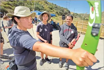  ?? Dan Watson/The Signal ?? (Above) Coach Jen So, left, demonstrat­es how to draw and aim the bow for beginners Yuri Gumatay, 13, center, and his father, Orlando, of Canyon Country, during the 2019 Olympic Day, held at SCV Archery in Canyon Country on Saturday.