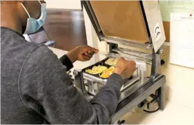  ?? STAFF PHOTO BY WYATT MASSEY ?? Bob Makazhu, a student at The University Of The South, prepares the Community Action Committee’s packaging machine last week in Sewanee.