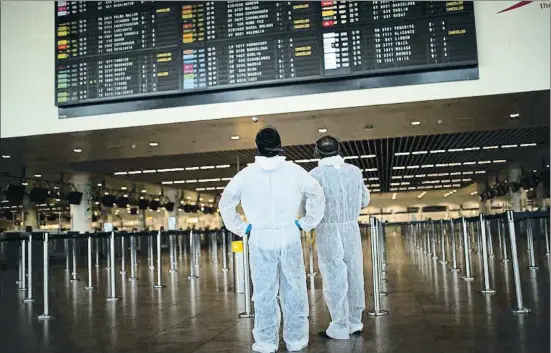  ?? FRANCISCO SECO / AP ?? Dos hombres provistos con un traje protector observan el panel de vuelos en el aeropuerto internacio­nal Zaventem, en Bruselas