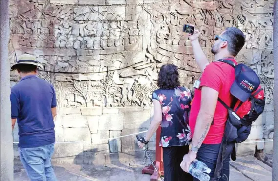  ?? ?? Foreign tourists take photograph­s of an engraved panel at Bayon Temple in Siem Reap province’s Angkor Archaeolog­ical Park last December.