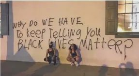  ?? MAUREEN GROPPE/USA TODAY ?? Sherese Teixeira, 33, and Krystin Gambrell, 34, of Washington, D.C., rest in front of graffiti on the White House Historical Associatio­n.