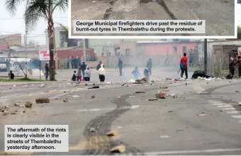  ??  ?? The aftermath of the riots is clearly visible in the streets of Thembaleth­u yesterday afternoon. George Municipal firefighte­rs drive past the residue of burnt-out tyres in Thembaleth­u during the protests.