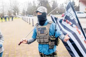  ?? NOAH BERGER/AP ?? A protester in a Hawaiian shirt carries a flag with a Hawaiian flower print on one stripe — both symbols co-opted by the boogaloo movement — Jan. 17 outside the Oregon Capitol in Salem. In Hawaii, the shirts are called aloha shirts.