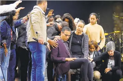  ?? K.C. ALFRED U-T ?? The Rock Church held a 20th Anniversar­y Service in Point Loma on March 1. Here, family members and others prayed for Pastor Miles Mcpherson and his wife Debbie, as they sit on a chair Miles found on the roof of the church 20 years ago.