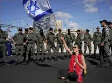  ?? ?? At right: A demonstrat­or waves the Israeli flag while seated on a highway Thursday while flanked by paramilita­ry border police.