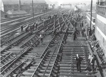  ?? Kiddermins­ter Railway Museum Collection ?? With Bristol (Temple Meads) in the background, in the first spring of a new era, that of the nationalis­ed railway, on 14 March 1948 a massive track relaying operation is ongoing outside the modern brick and concrete-built Temple Meads East signal box, the projecting bay of its first floor operating room just in view on the right. It was one of three power boxes installed in the 1930s to cope with a newly-enlarged station and using colour light signals; East box alone had 368 miniature levers. A double scissors crossover has been completed at the side of the railway and, after being bodily skidded transverse­ly by 160ft using manpower, it is now being slowly moved forward into position, hauled by wire ropes attached to two engines that are not shown in view, these working abreast on parallel tracks. Note the hand signals to the engine drivers.