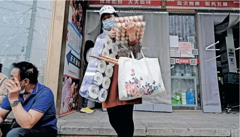  ?? | AFP ?? A WOMAN leaves a supermarke­t after buying food and household provisions in Beijing, yesterday. Fears of a hard Covid-19 lockdown sparked panic buying in Beijing as long queues formed in a large central district for mass testing ordered by the Chinese authoritie­s.