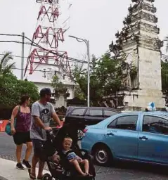  ??  ?? PELANCONG asing melintasi menara amaran tsunami di Kuta berhampira­n Denpasar di Bali, semalam. - AFP