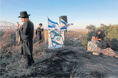 ?? AFP ?? Ultra-orthodox Jewish men pray as Israeli settlers gather on a hill next to the Palestinia­n town of Halhul, north of Hebron in the occupied West Bank on Monday.