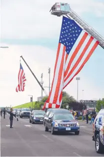  ??  ?? Las Cruces Fire Department ladder trucks hold flags above the roadway as a hearse approaches the Pan American Center ahead of the funeral service.