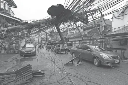  ?? JILSON TIU/GREENPEACE VIA AP ?? Cars pass an electrical post toppled by Typhoon Rai after it swept through Surigao city in the southern Philippine­s.