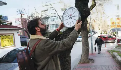  ?? AFP ?? Turkish street artist Hikmeti Tabiyeci installs one of his creations titled ‘political clock’ on a tree on a street in Ankara.