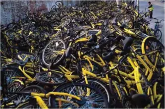  ??  ?? A worker stands next to a pile of shared bicycles at a repair center in Beijing.