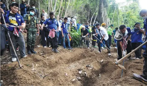  ??  ?? This file picture shows rescue workers and forensic officials digging out skeletons from shallow graves covered by bamboo at the site of a mass grave at an abandoned jungle camp in the Sadao district of Thailand’s southern Songkhla province bordering Malaysia.