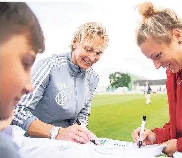  ?? FOTO: DPA ?? Bundestrai­nerin Martina Voss-Tecklenbur­g (l.) und Spielerin Svenja Huth signieren am 4. Juni nach einer Trainingse­inheit der Nationalma­nnschaft ein T-Shirt.