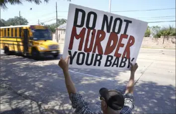  ?? LM Otero/Associated Press ?? David Trujillo holds a sign Thursday as a school bus drives by in front of a building housing an abortion provider in Dallas. Abortions resumed after a federal judge on Wednesday ordered Texas to suspend a new law that has banned most abortions in the state since September.