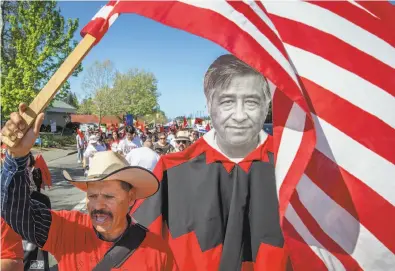  ?? Photos by Santiago Mejia / The Chronicle ?? Above: Guadalupe Suarez waves the flag next to a cutout of Cesar Chavez as farmworker­s march to honor the late labor leader and protest President Trump’s actions. Below: Ventura Longoria wears a Chavez button.