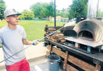  ?? JERRY DAVICH/POST-TRIBUNE ?? Brian Rock, co-owner of Elevated Pie Co., a mobile wood-fire pizza operation that opened last year, slides a hand-tossed gourmet pizza into the oven Thursday at an outdoor summer market in Hobart.