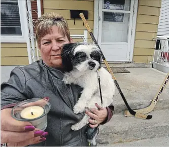  ?? CLIFFORD SKARSTEDT | EXAMINER ?? Cheryl Smith cuddles with her dog Panda on Tuesday at her front porch decorated with a pair of hockey sticks and a lit candle to honour the 15 people killed in the Humboldt Broncos hockey team bus crash Friday.