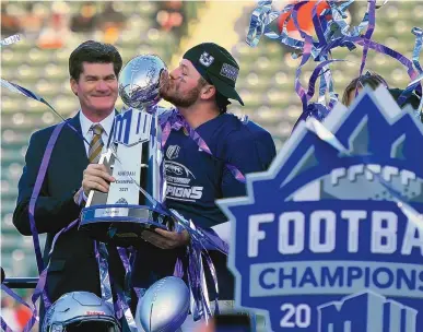  ?? JOHN MCCOY/ASSOCIATED PRESS ?? Mountain West Conference commission­er Craig Thompson, left, looks on as Utah State quarterbac­k Logan Bonner kisses the championsh­ip trophy after the Aggies defeated San Diego State in the Mountain West Conference championsh­ip game on Dec. 4, 2021, in Carson, California. Thompson calls realignmen­t “the elephant in the room.”