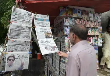  ?? — AFP photo ?? Pakistani residents read morning newspapers at a stall a day after the general election in Islamabad.