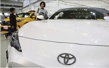  ?? — AP ?? Growth strategy: Visitors looking at a Toyota car at a showroom in Tokyo. Toyota has expanded EV developmen­t capabiliti­es since last year when it announced it would add fully electric vehicles to its product line-up.