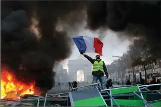  ?? The Associated Press ?? CHAMPS-ÉLYSÉES: A demonstrat­or waves the French flag on top of a burning barricade on the Champs-Élysées avenue with the Arc de Triomphe in the background during a demonstrat­ion Saturday in Paris. French police fired tear gas and water cannons to disperse demonstrat­ors, as thousands gathered in the capital and staged road blockades across the nation to vent anger against rising fuel taxes and Emmanuel Macron’s presidency.