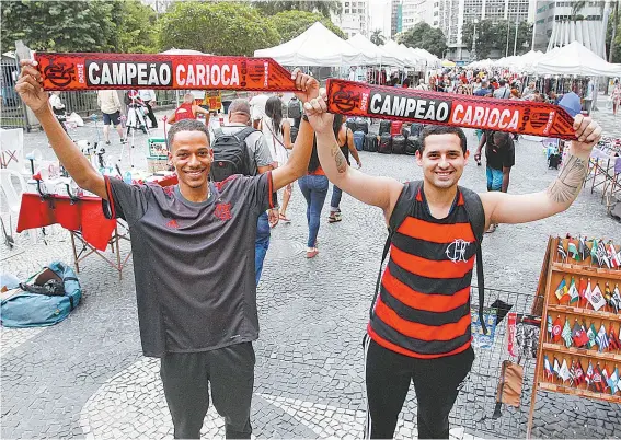  ??  ?? Os rubro-negros Marlon (E) e Pasquale exibem a faixa de campeão, no Largo da Carioca: confiança total no 35º título estadual do Flamengo
