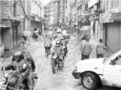  ??  ?? Nepali people transit along a water logged street in Patan, south of Kathmandu. — AFP photo