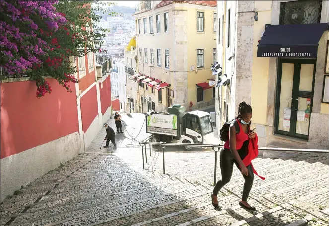  ??  ?? In this photo taken on June 24, a woman wearing a face mask walks past workers washing the street in Lisbon’s old center. Portugal avoided the dramatic numbers of infections and deaths recorded by some other European Union
countries during the early months of the coronaviru­s outbreak but since ending its state of emergency and lockdown at the end of April, its total of officially recorded new infections has remained stubbornly high. (AP)