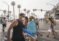  ?? Apu Gomes / AFP / Getty Images ?? People cross the street in the Orange County community of Huntington Beach, with only some wearing masks.