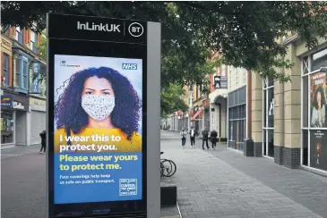  ?? AFP ?? People walk by an electronic billboard displaying a government message reminding people to wear face masks as a precaution against spreading Covid-19 in Leicester on Monday.