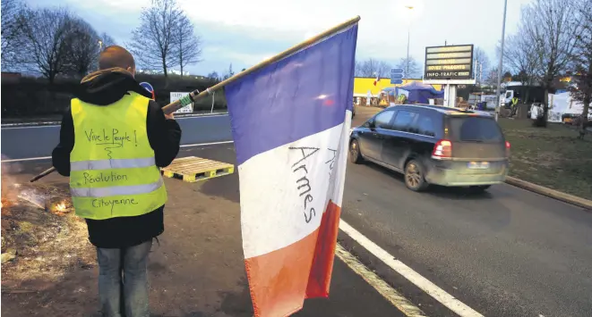  ??  ?? A protester, wearing a yellow vest, holds a French flag, in Fontaine-Notre-Dame, Dec. 4.
