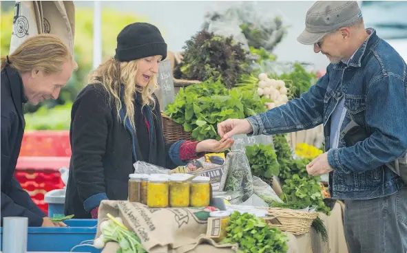  ?? ARLEN REDEKOP/PNG ?? Ilana Guslits of Sole Food Street Farm serves a customer at the Downtown Farmers Market at Queen Elizabeth Theatre Plaza on Thursday. The bad spring weather has put many crops behind schedule but hasn’t kept the customers away.