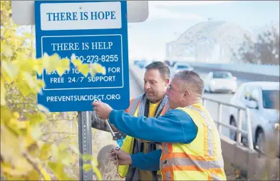  ?? PATRICK RAYCRAFT/HARTFORD COURANT ?? Middletown public works employees Joe Barone, right, and Sebastian Annino install suicide prevention signs Friday morning on the Arrigoni Bridge in Middletown. The state DOT approved the signs as an interim step as it prepares to install fencing and other measures as part of a major bridge constructi­on project starting next year. Suicide prevention officials said signage can be a deterrent just by making someone think about the step they’re about to take.