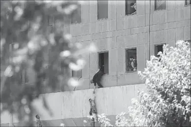  ??  ?? Een mam geeft vanuit het raam van het Iraans parlements­gebouw een kind aan een security guard na de aanval in Tehran, Iran.