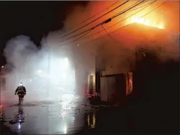  ?? Wally Skalij Los Angeles Times ?? BUSINESSES ALONG Melrose Avenue in Los Angeles’ trendy Fairfax district took stock Sunday after a night of civil unrest. Above, a firefighte­r walks behind a building ablaze on Melrose on Saturday night.