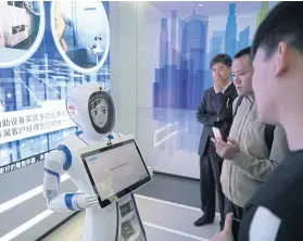  ??  ?? Bank customers speak with a robot at an automated branch in Shanghai.