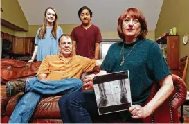  ?? Wade Payne / Associated Press ?? Leslie Kurtz shows a print of an X-ray of her ankle while she’s in her home in Knoxville, Tenn., with husband Bart Bartram, daughter Rainey and son Rio.