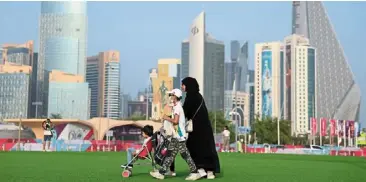  ?? ?? Stroll in the park: a mother and her children arrive at the opening of the FIFA Fan Festival as the doha skyline is seen in the background.