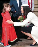  ??  ?? Down with the kids: Meghan accepts a gift of flowers from a young girl