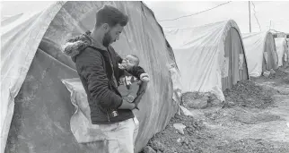  ?? REUTERS ?? Taama al-owais, carries his three-month-old son as he stands in front of his tent in an informal camp in the town of Balad, Iraq.