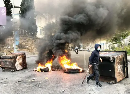  ?? Reuters ?? A demonstrat­or walks past burning tires and garbage bins blocking a road in Beirut during Thursday’s protest against mounting economic hardships.