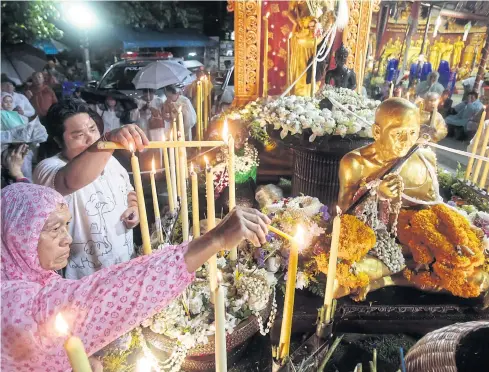  ?? PHOTOS BY PATIPAT JANTHONG ?? Despite the rain, villagers light candles to pay respect to a Buddhist monk statue during the Tiew Khuen Doi festival as they climb the steps to Doi Suthep in Chiang Mai to commemorat­e Visaka Bucha Day yesterday.