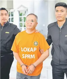  ??  ?? The suspect clad in MACC orange lock-up attire and handcuffed, arriving at the Putrajaya Magistrate­s’ court. — Bernama photo